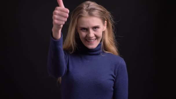 Νεαρή ξανθιά μοντέλο σε μπλε πουλόβερ βάζει το δάχτυλό της για να δείξει όπως και σεβασμό χαρούμενα στην κάμερα σε μαύρο φόντο. — Αρχείο Βίντεο