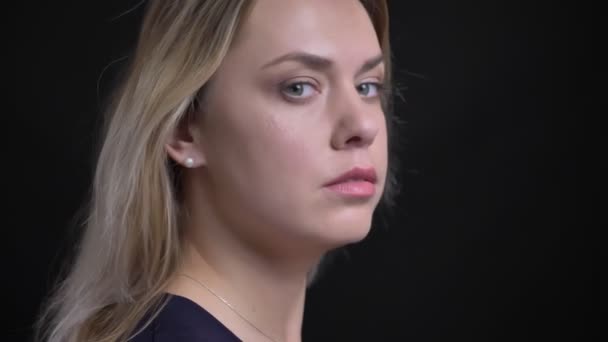 Profile shot middle-aged blonde businesswoman in blue blouse turns to camera and watches seriously into it on black background. — Stock Video