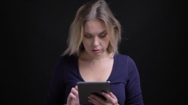 Kepçe yaka ile mavi bluz sarışın iş kadını siyah arka planda tablet içine düşünceli izliyor.