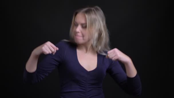 Счастливая блондинка средних лет в голубой блузке активно и эмоционально танцует на черном фоне . — стоковое видео