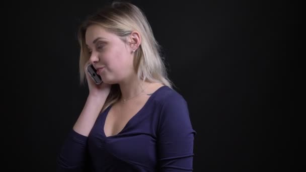 Blond affärskvinna i blå blus med Scoop urringning med informell voicecall på smartphone på svart bakgrund. — Stockvideo