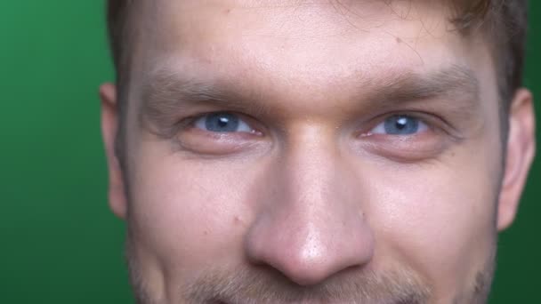 Close-up eye portrait of young brunette sportsman smiling joyfully into camera on green background. — Stock Video