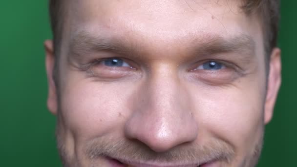 Close-up oog portret van jonge brunette sportman glimlachend gelukkig in de camera op groene achtergrond. — Stockvideo