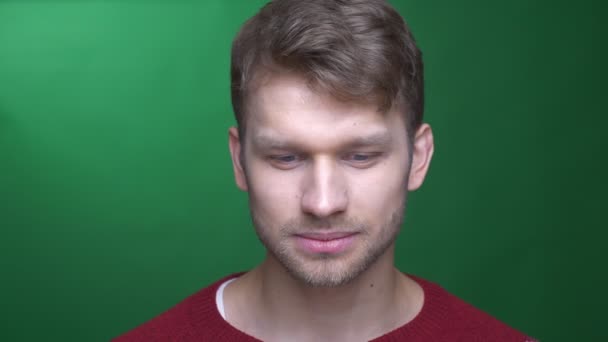 Happy young brunette sportsman watching with shy smile into camera on green background. — Stock Video