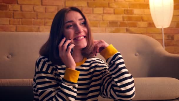 Closeup portrait of young pretty girl having a phone call and talking cheerfully sitting on the floor in a cozy apartment indoors — Stock Video