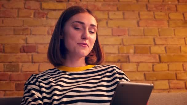 Closeup portré fiatal csinos lány, amelynek videohívás a tabletta és beszél vidáman ül a kanapén egy hangulatos lakásban beltéri — Stock videók