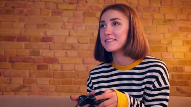 Closeup portrait of young pretty girl playing video games using the game console and being happy sitting on the couch in a cozy apartment indoors — Stock Video