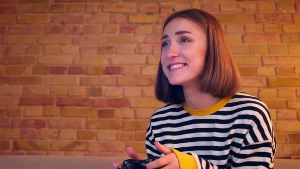 Primer plano retrato de la joven chica alegre jugando videojuegos utilizando la consola de juegos entretenido sentado en el sofá en un acogedor apartamento en el interior — Vídeo de stock