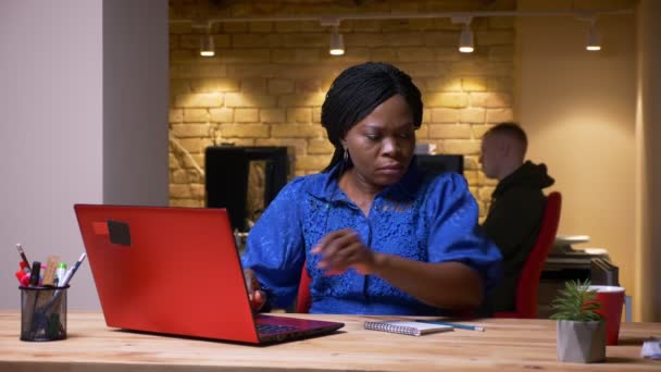 Съемки крупным планом взрослой африканской предпринимательницы, использующей ноутбук и пьющей кофе в офисе в помещении — стоковое видео