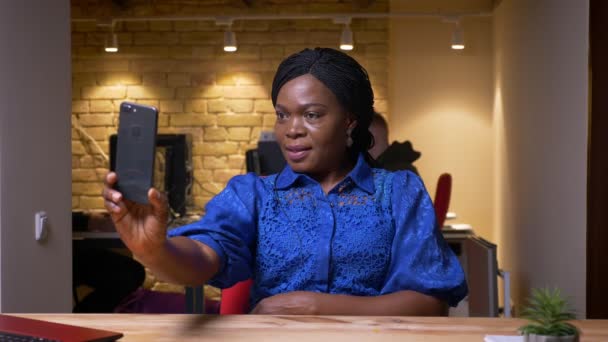 Крупный план съемки взрослой африканской бизнесвумен делает селфи по телефону и позирует перед камерой в офисе в помещении — стоковое видео