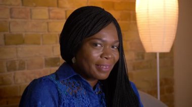 Rahat bir dairede kanepede oturan kamera bakarak neşeyle gülümseyen yetişkin afro-amerikan kadın Closeup ateş