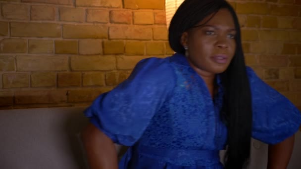 Close-up shoot van volwassen Afro-Amerikaanse vrouwelijke TV kijken met gerichte nieuwsgierige uitdrukking zittend op de Bank binnenshuis — Stockvideo
