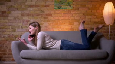 Genç çekici kafkas esmer kadın rahat bir dairede kapalı kanepede yatan bir telefon görüşmesi olan Closeup portre