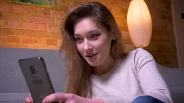 Genç çekici kafkas esmer kadın telefonla sosyal medya tarama closeup portre rahat bir dairede kapalı yerde oturarak