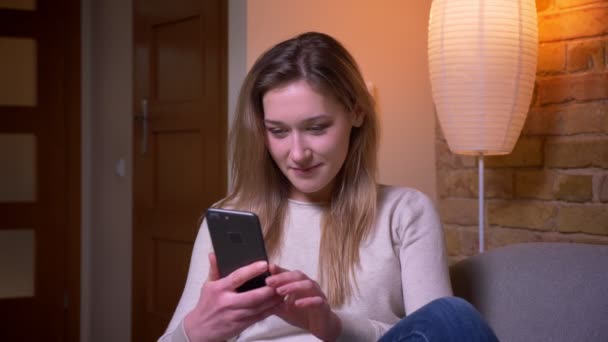 Close-up portret van jonge aantrekkelijke Kaukasische brunette vrouw met behulp van de telefoon en het tonen van groen scherm naar camera plaatsings op de vloer binnenshuis in een gezellige flat — Stockvideo