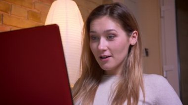 Genç çekici sevimli esmer kadın dizüstü bilgisayarda bir film izlerken ve rahat bir daire içinde kanepede oturarak eğlenceli ve neşeli olmak Closeup portre