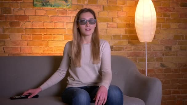 Potret close up dari wanita muda berambut cokelat kaukasia yang menarik menonton film horor 3D di TV dan merasa takut duduk di sofa di dalam ruangan yang nyaman — Stok Video