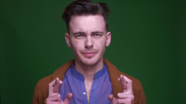 Closeup shoot of adult attractive man having his fingers crossed and begging hopefully looking at camera with background isolated on green — Stock Video