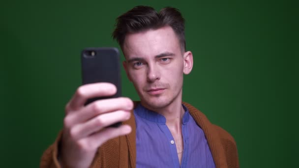 Съемки крупным планом взрослого привлекательного мужчины, делающего селфи по телефону с изолированным на зеленом фоне — стоковое видео