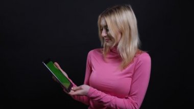 Tablet kullanarak genç güzel sarışın kadın Closeup ateş ve siyah izole arka plan ile kameraya yeşil renk ekran gösteren