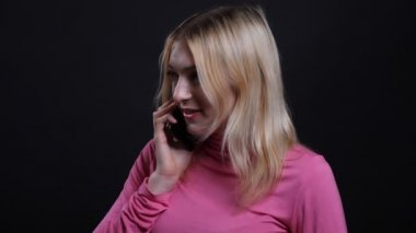 Bir telefon görüşmesi olan ve siyah izole arka plan ile neşeyle konuşan genç güzel sarışın kadın Closeup ateş