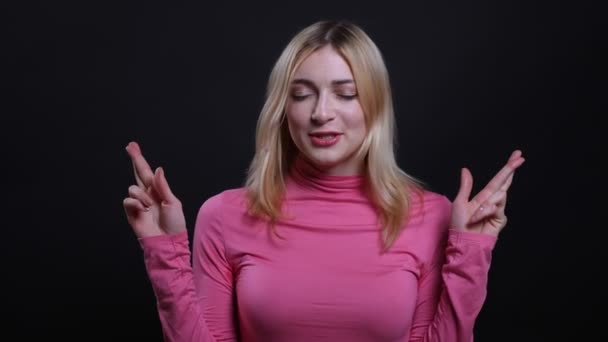 Съемки крупным планом молодой красивой блондинки со скрещенными пальцами и беспокойным взглядом на камеру с изолированным на черном фоне — стоковое видео