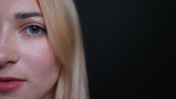 Closeup half face shoot of young pretty blonde caucasian female looking straight at camera with background isolated on black — Stock Video