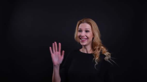 Портрет крупным планом взрослой привлекательной рыжей женщины, машущей привет и счастливо улыбающейся на фоне, изолированном от черного — стоковое видео