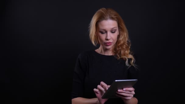 Närbild porträtt av vuxna attraktiv rödhårig kvinna använda tabletten med bakgrund isolerad på svart — Stockvideo