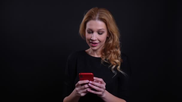 Крупним планом портрет дорослої привабливої рудої жінки, використовуючи телефон перед камерою з фоном ізольовані на чорному — стокове відео
