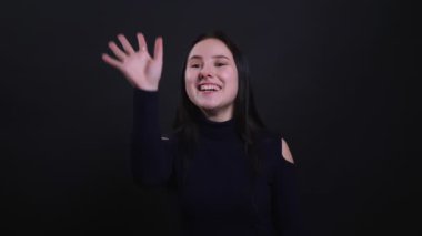 Genç çekici esmer kadın hi sallayarak ve siyah izole arka plan ile mutlu bir şekilde gülümseyen Closeup portre