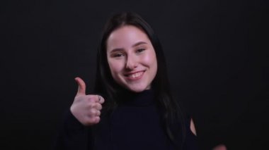 Siyah arka plan izole kamera bakarak güvenle gülümseyerek bir başparmak gösteren genç çekici esmer kadın Closeup portre