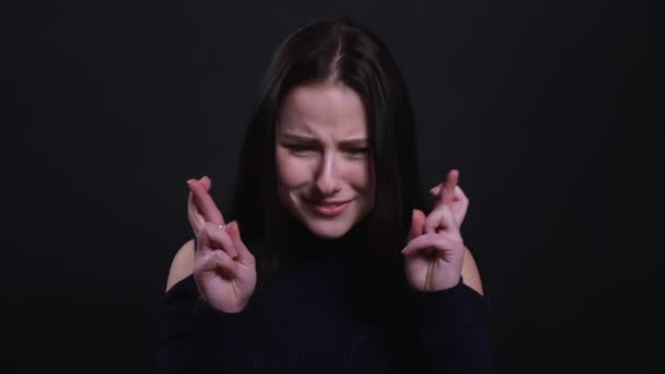 Closeup portrait of young attractive brunette femalehaving her fingers crossed and being anxious with background isolated on black — Stock Video