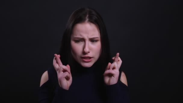 Closeup portrait of young attractive brunette femalehaving her fingers crossed and being anxious praying and begging with background isolated on black — Stock Video