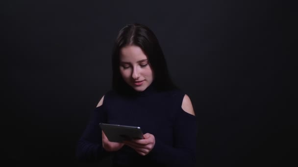 Primer plano retrato de joven atractiva morena femenina utilizando la tableta con fondo aislado en negro — Vídeos de Stock