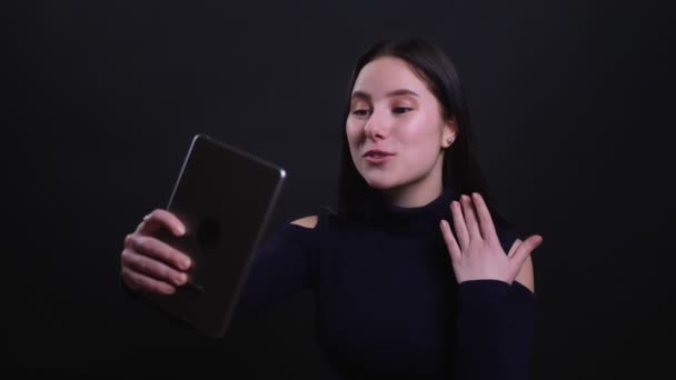 Close-up portret van jonge aantrekkelijke brunette vrouw met een video-oproep op de Tablet met achtergrond geïsoleerd op zwart — Stockvideo