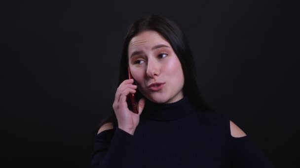 Close-up portret van jonge aantrekkelijke brunette vrouw met een telefoongesprek glimlachend vrolijk met achtergrond geïsoleerd op zwart — Stockvideo