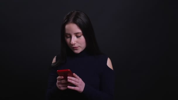 Retrato de close-up de jovem morena atraente usando o telefone na frente da câmera com fundo isolado em preto — Vídeo de Stock