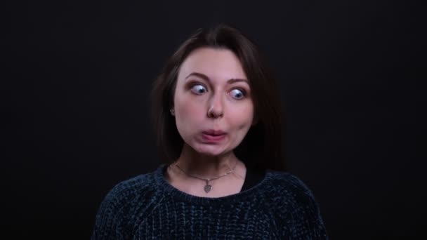 Closeup retrato de adulto bela morena caucasiana do sexo feminino fazendo expressões faciais engraçadas e divertido olhando para a câmera com fundo isolado no preto — Vídeo de Stock