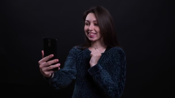 Zbliżenie portret dorosłego pięknego kaukaski brunetka femalehaving a wideo rozmowa na telefon wesoło rozmawia z tłem na białym tle na czarno — Wideo stockowe
