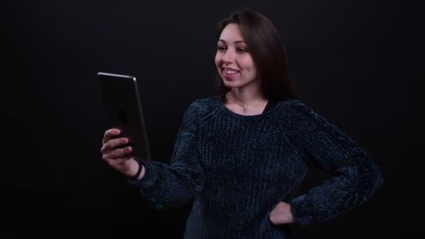 Primer plano retrato de adulto hermosa morena caucásica hembra teniendo una videollamada en la tableta con fondo aislado en negro — Vídeo de stock