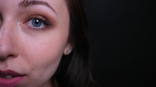 Closeup napůl obličej portrét mladé krasotické Brunetky, která se dívá přímo na kameru s pozadím izolovaným na černém — Stock video