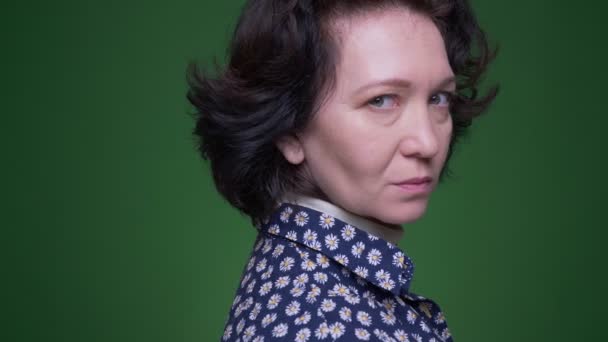 Closeup portrait of old caucasian brunette female turning and looking at camera with background isolated on green — Stock Video