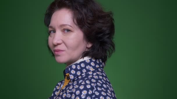 Крупный план портрет старой брюнетки кавказского цвета, поворачивающейся и глядящей на камеру, радостно улыбающейся на фоне изолированного на зеленом фоне — стоковое видео