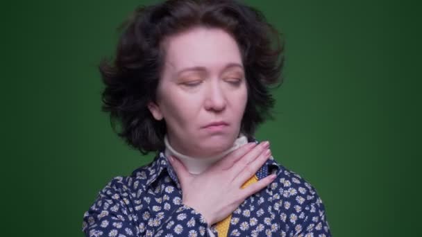Closeup portrait of old caucasian brunette femalehaving a sick throat and being ill coughing with background isolated on green — Stock Video