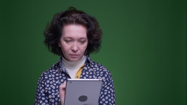 Close-up portret van oude Kaukasische brunette vrouw met behulp van de Tablet en het tonen van blauwe Chroma scherm naar camera met achtergrond geïsoleerd op groen — Stockvideo