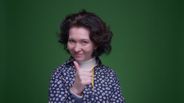 Closeup portrét staré kavkazské bruneté ženy ukazující palec vzhůru s úsměvem na kameře s pozadím izolovaným na zeleném — Stock video
