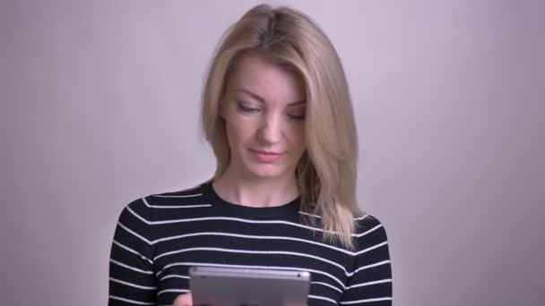 Primer plano retrato de adulto atractivo rubia caucásica hembra utilizando la tableta y sonriendo con fondo aislado en blanco — Vídeos de Stock