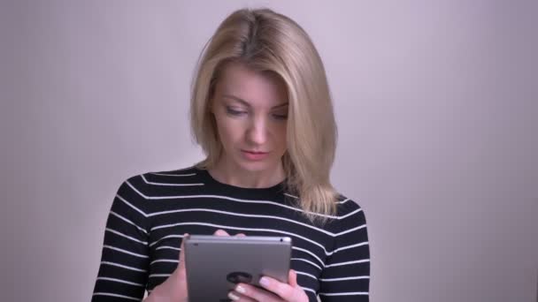 特写肖像成人有吸引力的金发白人女性使用平板电脑和看着相机微笑的背景孤立在白色 — 图库视频影像