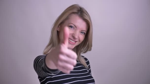 Close-up retrato de adulto atraente loira caucasiano fêmea mostrando um polegar para cima sorrindo olhando para a câmera com fundo isolado no branco — Vídeo de Stock